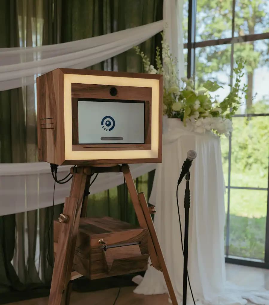 Borne de livre d'or vidéo Chronobooth en bois, avec son cadre lumineux, installée près d'une composition florale blanche dans une salle de réception